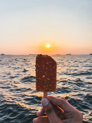 Hand holding an ice cream with the Aegean Sea in the background during sunset, Izmir, Turkey
