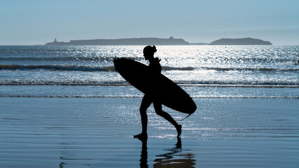 Silhouette of an unidentified man with a surf board, walking in the beach of Essaouira, Morocco,...