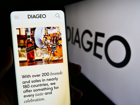 Stuttgart, Germany - 11-22-2023: Person holding smartphone with web page of British alcoholic beverage company Diageo plc in front of logo. Focus on center of phone display.