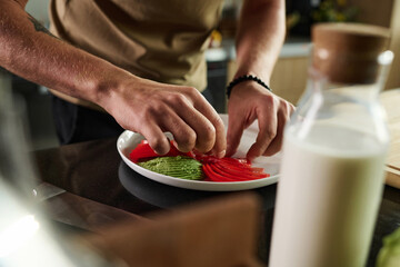 Closeup of hands of unrecognizable man placing sliced tomato nearby slices of avocado on plate