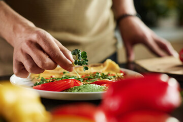 Closeup of hand of unrecognizable man putting microgreen on dish made of sliced vegetables and...