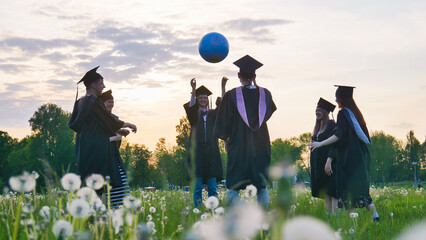 Graduates in costume playing with a ball at sunset.