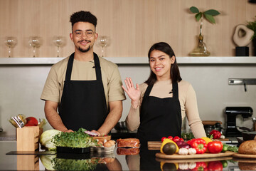 Waist up shot of smiling young middle eastern man and happy hispanic woman looking at camera while posing by kitchen counter - Powered by Adobe