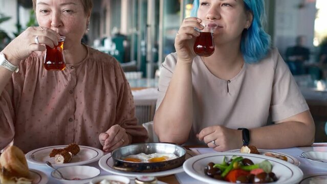 two women are laughing and talking as they eat, clearly enjoying each other's company. Turkish Breakfast, Sunday breakfast or brunch with feta cheese and eggs, Turkish meal served in restaurant