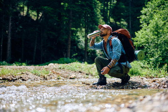 Young hiker drinks water from mountain creek.