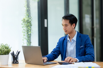 Smiling asian businessman using laptop computer at office. Confident Asia businessman sitting happily in the office.