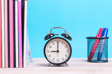 A pile of Magazine books and with coloured pen and alarm clock on a wooden with blue background - Powered by Adobe