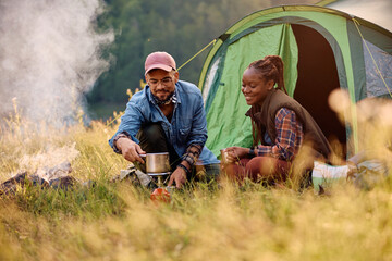 Happy couple of campers preparing tea on on portable gas burner in nature.