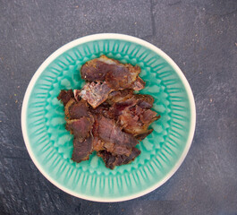 Plain green bowl with dried meat on slate 