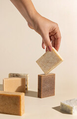 Hand keeps natural beige and brown soap bars on light beige, hard shadows