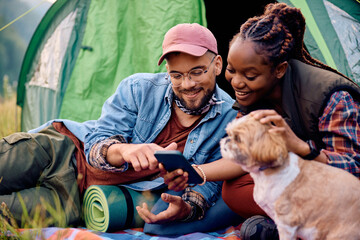 Happy couple with dog using cell phone while camping in nature.