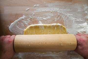 M&uuml;rbeteig mit einem Rollholz auf einem Tisch ausrollen