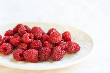 Fresh, ripe raspberries on a white plate, set against a white tablecloth. Perfect for a healthy snack or dessert.
