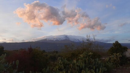 Ampio panorama dell'Etna al tramonto, con nuvole colorate e fichi d'india in primo piano.
