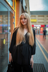 Portrait of a young beautiful blonde girl in dark clothes in an urban environment.