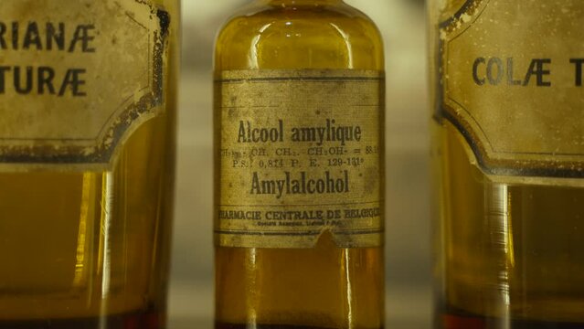 Old medical jar made of colored glass with amyl alcohol. Medical and household solvent with old worn label on glass flask standing on shelf among other solutions, handheld shot.