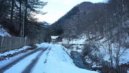 A frozen road winding along a river. The valley lies inside a mountainous area. A small countryside...
