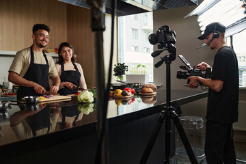 Medium long shot of smiling middle eastern man and happy hispanic woman cooking while being filmed...
