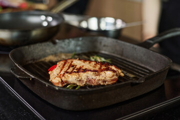 Closeup of cooked steak in grill pan with herbs around, focus on meat
