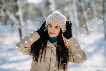 Portrait of a beautiful girl in winter clothes standing in a winter park on a sunny day and smiling. The winter vacation. Copy space.