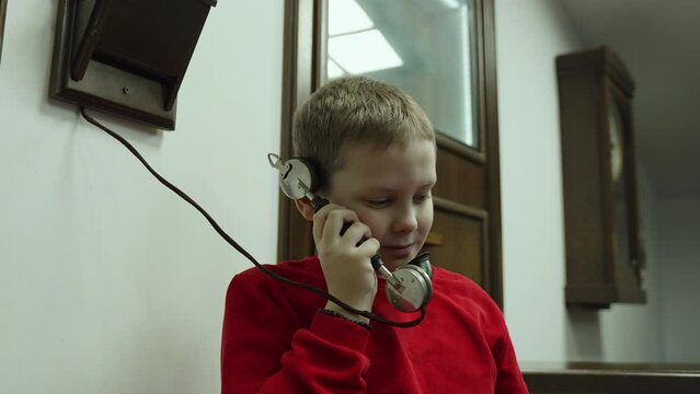 Portrait of european boy attentively listening to interlocutor in ancient telephone receiver. Alpha generation studies world history and familiarization with old communication technologies.