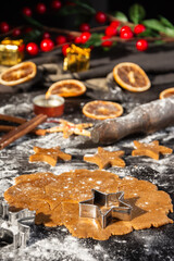 Close-up of gingerbread cookie dough for Christmas with star molds, cinnamon and oranges on dark table with flour, vertical