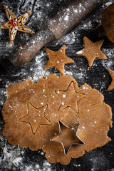 Aerial view of gingerbread cookie dough with star molds on dark table with flour, vertical