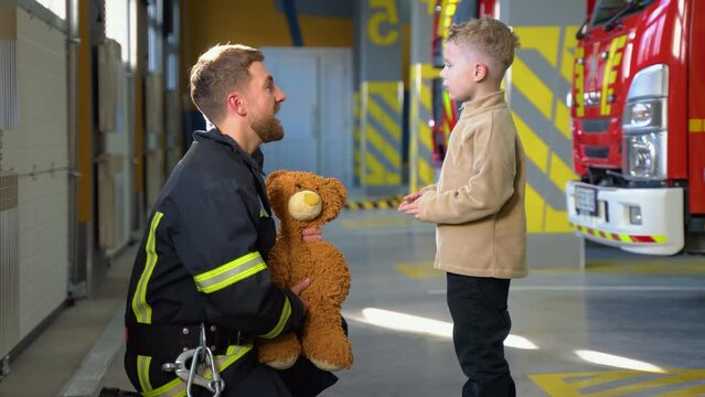 Firefighter and little boy at fire station. Fireman teaches a little boy fire safety regulations