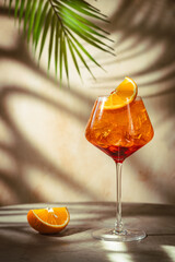 Glass of Aperol spritz cocktail with fresh oranges and palm leaves on beige background. natural light and shadows