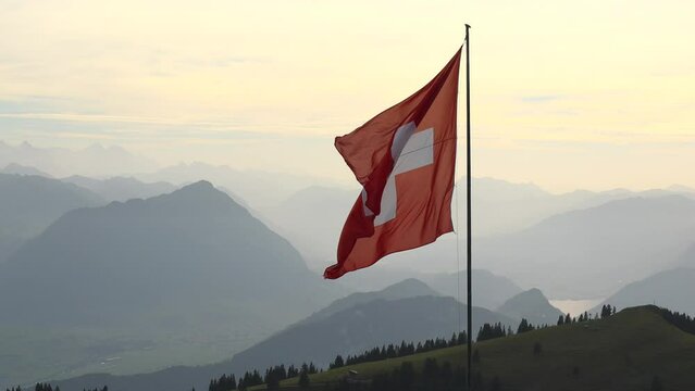 A large swiss flag evolves against the background of the swiss alps, the swiss flag on top of the mountain. The wind develops the flag.
