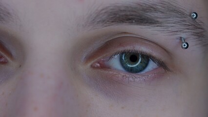 Eye of young guy with eyebrow piercing macro shot. Enlarged pupils, due to prolonged use of...