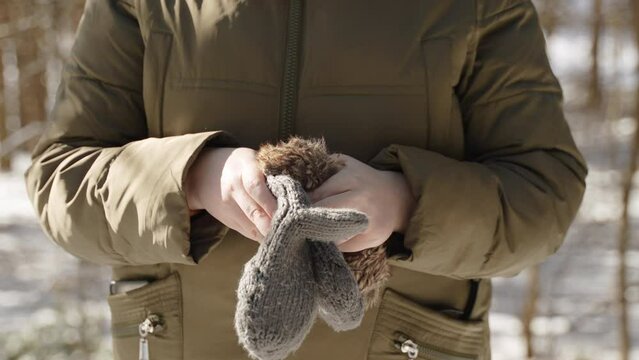 Caucasian european woman puts knitted mittens on her palms in cold winter. Close up of bare hands with mittens on frosty sunny morning. Protection from hypothermia and frostbite in winter season.