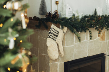 Cozy stockings hanging on mantel in modern farmhouse living room. Rustic christmas fireplace with warm knitted stockings and stylish decoration on fir branches. Atmospheric winter holiday
