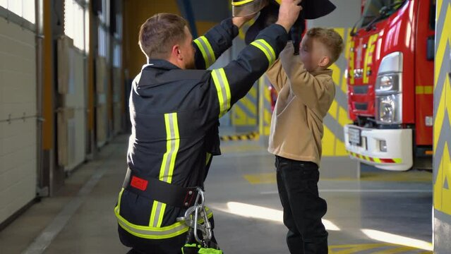 Friendly firefighter puts a protective helmet to a little boy