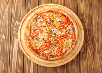 delicious pizza with chicken, mushrooms, cheese, tomatoes and corn on a wooden background