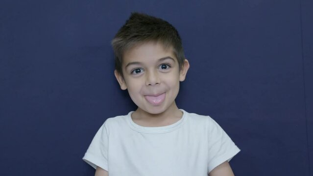 Little caucasian boy shows tongue and dance funny dance in slow motion, isolated on blue background. High quality 4k footage