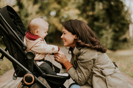 Young woman with cute baby girl in baby stroller at the autumn park