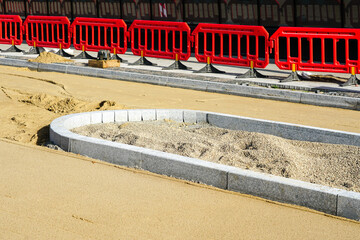 Street rebuilding view, gravel surface, concrete curbs, red plastic temporary safety barriers