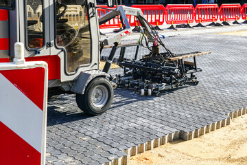 Paving block laying machine on new pavement, red plastic barriers, warning sign, repaved place