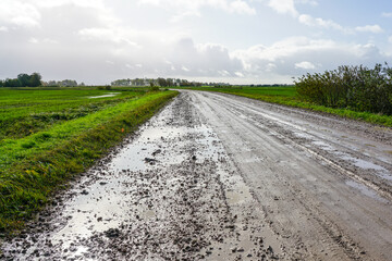 Muddy dirty rural gravel road with puddles of water after rain