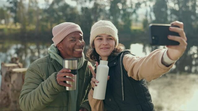 Selfie, hiking and an interracial couple in the forest together for travel, freedom or adventure in nature. Coffee, camping or experience with a man and woman posing for a photograph in the woods