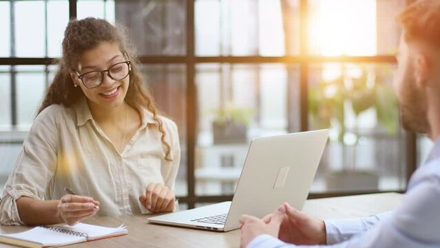 woman in glasses receives a client sitting at a laptop
