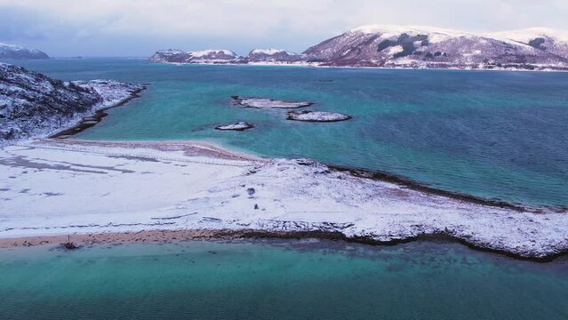 Aerial view around a sand beach with snow covered mountain background, on sunny winter Sommaroy island, Norway