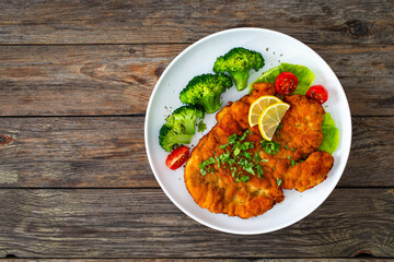 Crispy breaded fried chicken cutlet with boiled broccoli and fresh vegetables on wooden table
 - obrazy, fototapety, plakaty