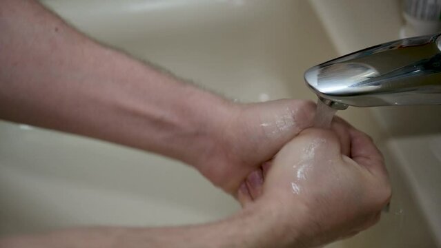 A man lathers his hands with soap under the running water of the bathroom sink
