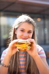 Teenage girl eating a burger at the outside restaurant
