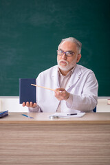 Old male teacher in front of green board