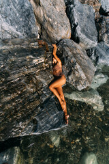 A beautiful young, sensual woman in a swimsuit is lying on the rocks by the sea.