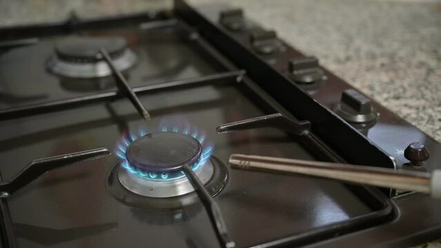 A male hand elevates the kitchen stove gas knob, ignites it with the kitchen lighter, and subsequently turns off the kitchen stove gas.

