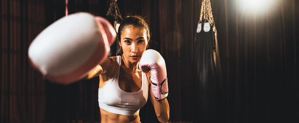 Asian female Muay Thai boxer punch fist in front of camera in ready to fight stance posing at gym...